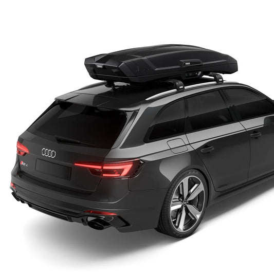 A black Audi station wagon shown from a rear three-quarter angle on a white studio background, fitted with a black roof-top cargo box.