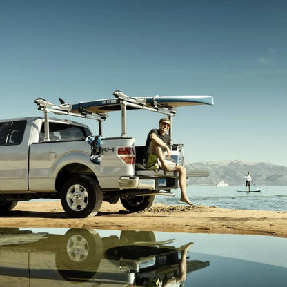 Thule Xsporter Pro setup on a white pickup truck parked by water, loaded with surfboards, with person looking happy