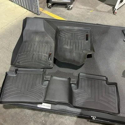 Set of black car floor mats on a concrete floor.