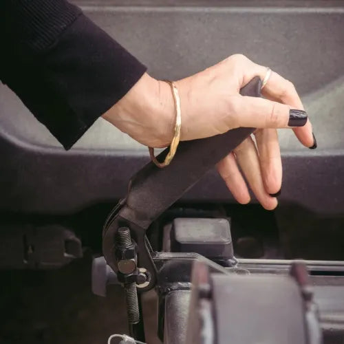 Hand with black nail polish holding a tool near car engine components