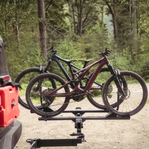 Two bicycles on a bike rack attached to a vehicle in a forest setting