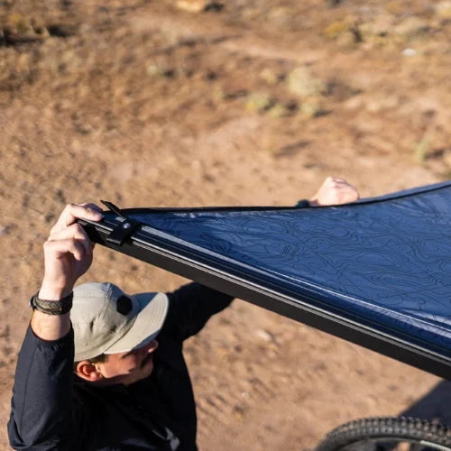 Close-up of Yakima OverNOut 270 rooftop awning fabric and mounting hardware during setup on overlanding vehicle, highlighting durable materials, secure construction, and premium outdoor camping shelter design