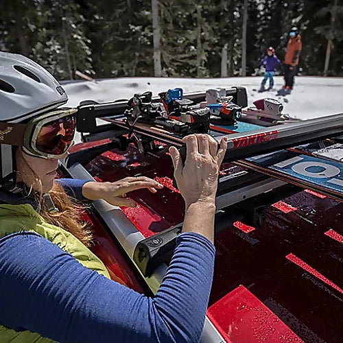 Woman loading skis onto Yakima FreshTrack roof rack on snowy day.