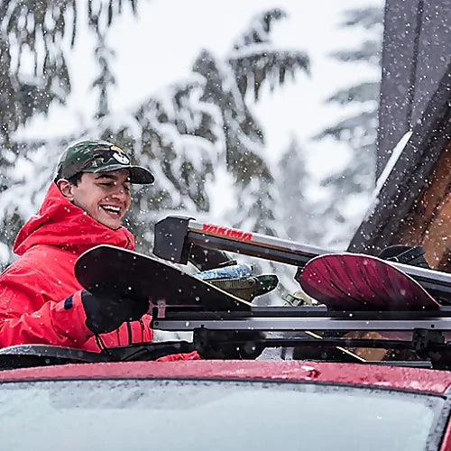 Snowboarder securing boards onto Yakima FreshTrack ski rack in winter snow.