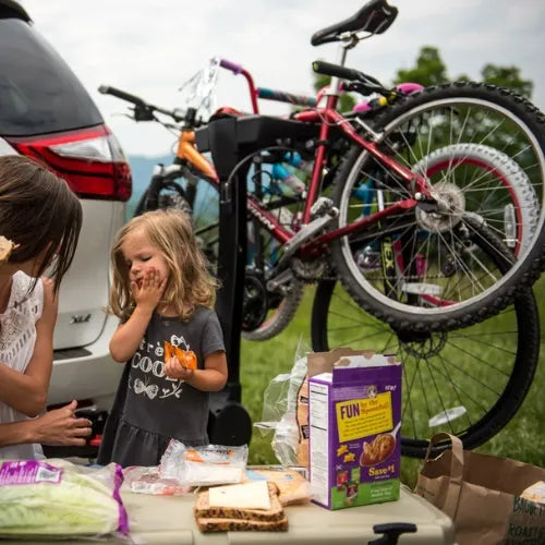 Two children at a picnic table with bicycles and a car in the background