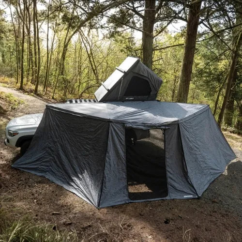 Portable roof top tent attached to a vehicle in a forest setting