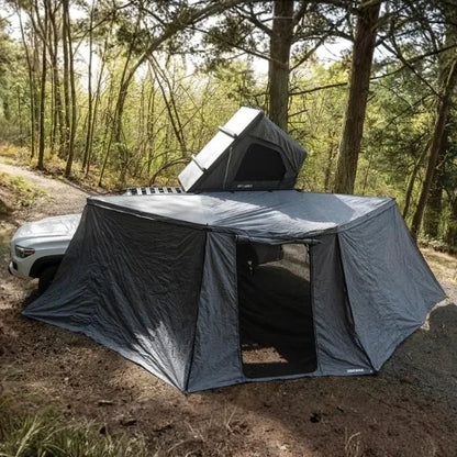 Portable roof top tent attached to a vehicle in a forest setting