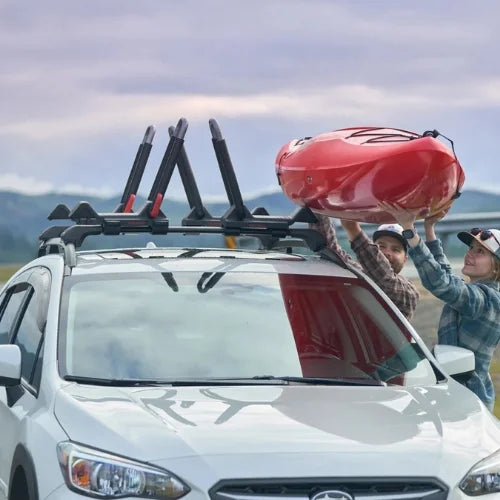 Two people loading a red kayak onto a car with a roof rack.