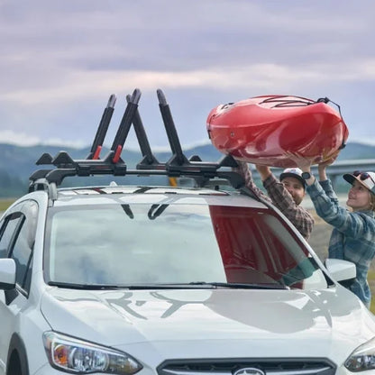 Two people loading a red kayak onto a car with a roof rack.