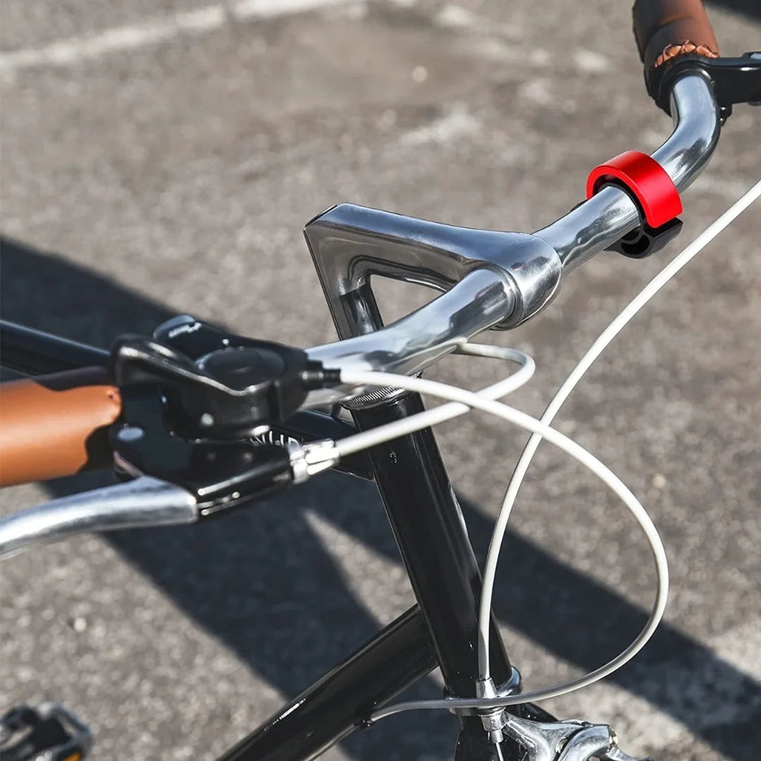 Red Q-shaped bicycle bell mounted on bike handlebars outdoors
