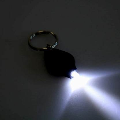 AO mini flashlight keychain turned on, emitting bright white light in the dark
