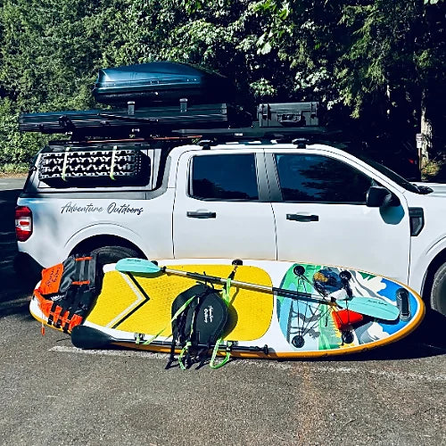 Paddleboards and gear mounted on a truck with rooftop tent and aluminum roof bars