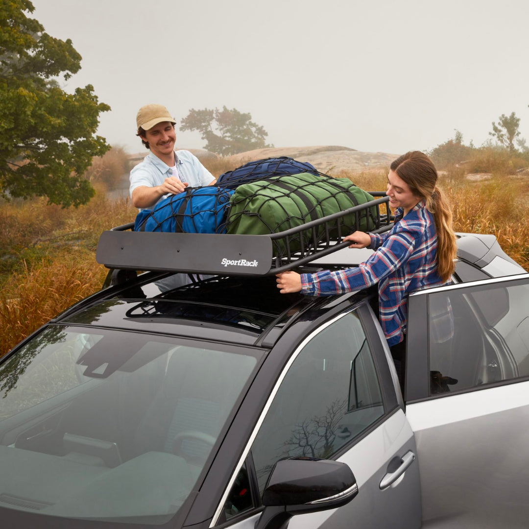 Low angle view of Vista Roof Basket filled with travel and camping gear on SUV. Two people fixing net over the basket to secure the gear in it. 