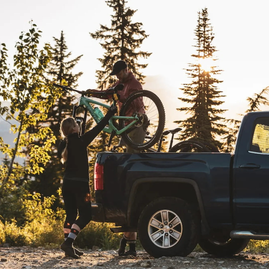 Man standing on his truck and lifting two bikes out of Swagman Paramount Tailgate Pad. He is reaching them to a women