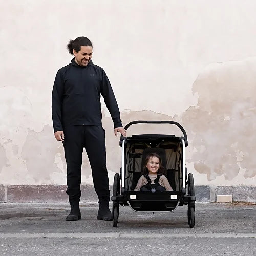 Parent and child standing with Thule Chariot Cross 2 Double Faded Khaki stroller showing comfort and family outdoor use
