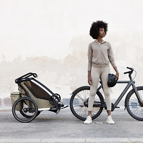 Lifestyle image of Thule Chariot Cross 2 Double Faded Khaki attached to a bicycle with parent preparing for urban ride