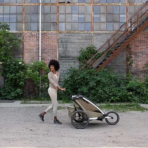 Woman pushing Thule Chariot Cross 2 Double Faded Khaki stroller outdoors showing all-terrain capability and style