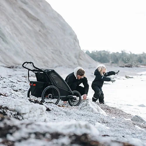 Thule Chariot Sport 2 on beach terrain with parent and child exploring outdoors showcasing all-terrain capability