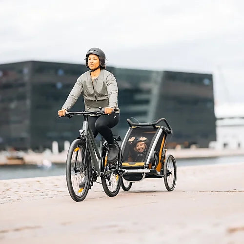 Parent biking with Thule Chariot Sport 2 trailer attached, illustrating safe family cycling and outdoor adventure use