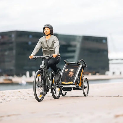 Parent biking with Thule Chariot Sport 2 trailer attached, illustrating safe family cycling and outdoor adventure use