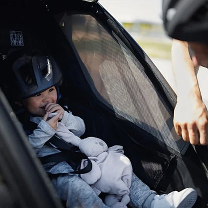 Child seated inside Thule Chariot Sport Single with helmet and mesh window ventilation