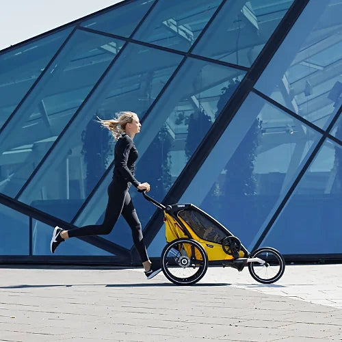 Woman running outdoors with Thule Chariot Sport Single jogging stroller in yellow during urban workout