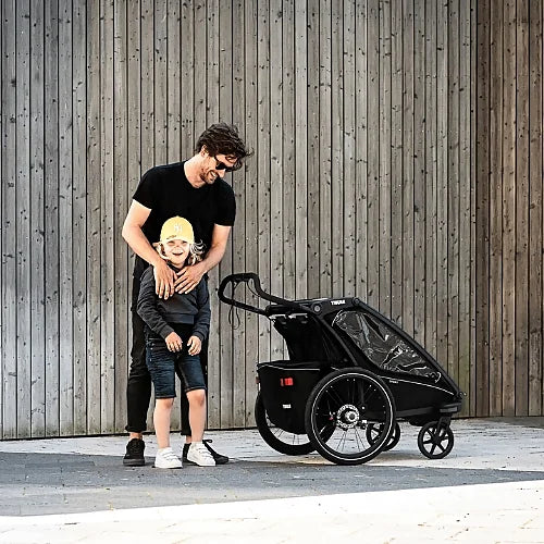 Parent with child using Thule Chariot Sport Single stroller outdoors on paved surface