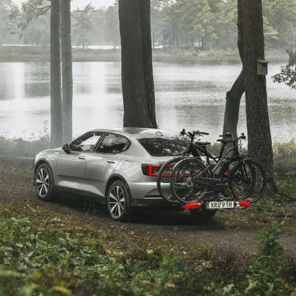 Sedan with Thule Epos hitch bike rack carrying two bikes in scenic forest setting