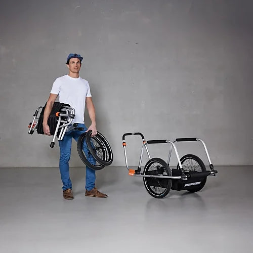 Person carrying folded Thule Reacha Sport trailer frame and wheels, showing compact and lightweight transport design