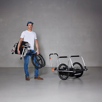 Person carrying folded Thule Reacha Sport trailer frame and wheels, showing compact and lightweight transport design