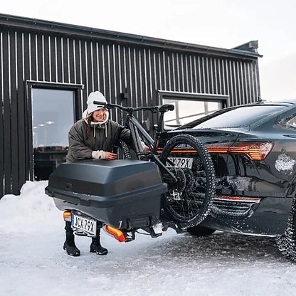 Thule Santu Hitch Cargo Box attached to car with Thule Epos bike rack in snowy winter setting, person loading bicycle and gear