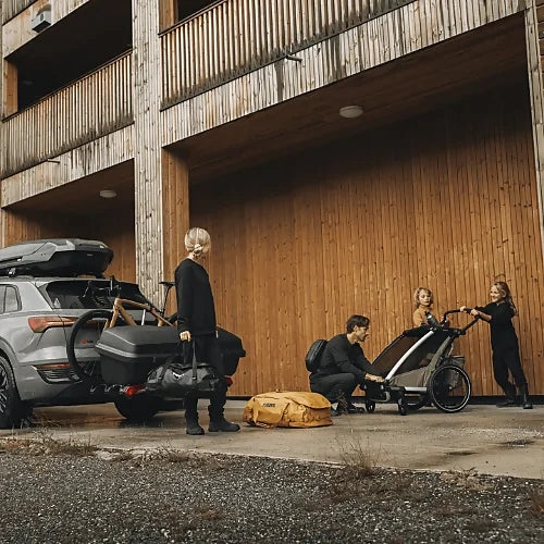 Family loading Thule Santu Hitch Cargo Box with stroller and bikes in parking area