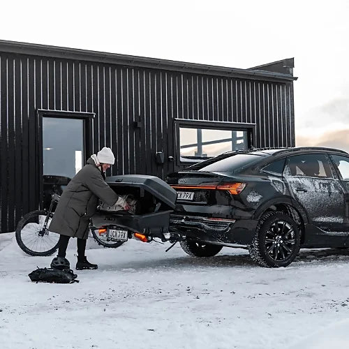 Person loading Thule Santu Hitch Cargo Box on a vehicle in snowy conditions outside a cabin