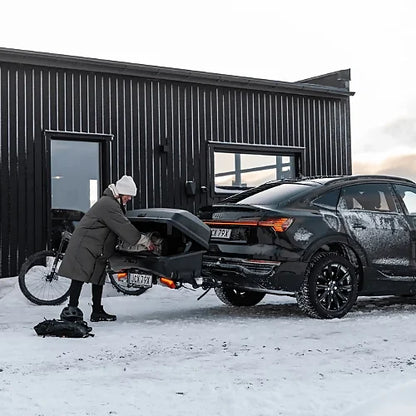Person loading Thule Santu Hitch Cargo Box on a vehicle in snowy conditions outside a cabin