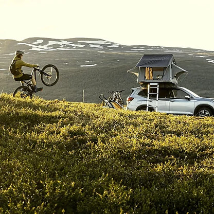 Thule Tepui Ayer 2 rooftop tent on SUV parked in mountain landscape with cyclist riding nearby