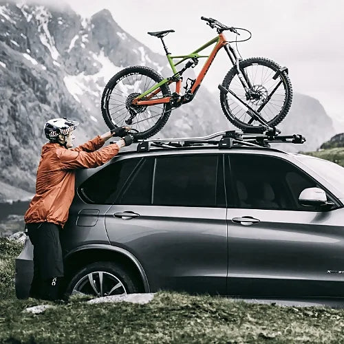 Rider securing mountain bike onto Thule UpRide rack on SUV in scenic backdrop