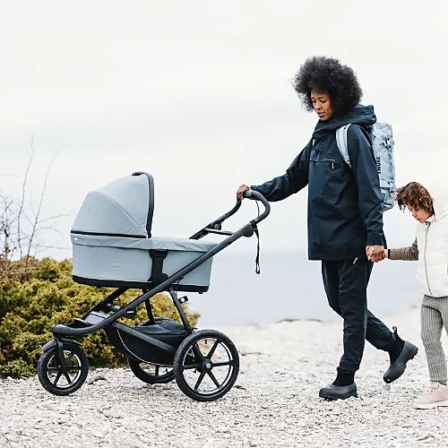 Parent pushing Thule Urban Glide 3 all-terrain stroller with bassinet on rocky outdoor trail