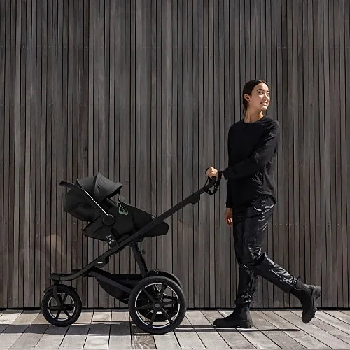 Parent pushing Thule Urban Glide 3 black all-terrain stroller along wooden wall background