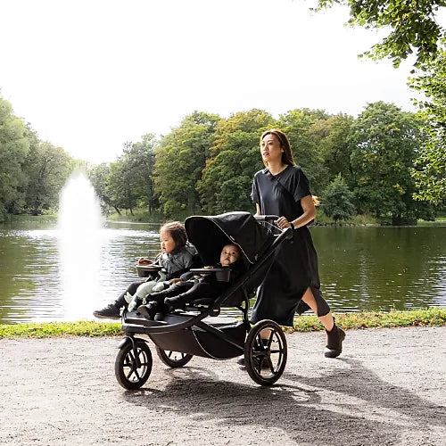 Parent jogging with the Thule Urban Glide 3 double stroller carrying two children beside a lakeside trail