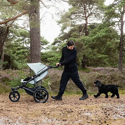 Parent pushing Thule Urban Glide 3 stroller on forest trail while walking a dog