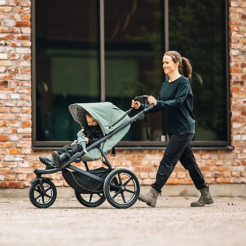 Parent pushing Thule Urban Glide 3 with toddler seated outdoors on paved surface
