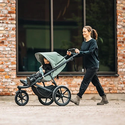 Parent pushing Thule Urban Glide 3 with toddler seated outdoors on paved surface