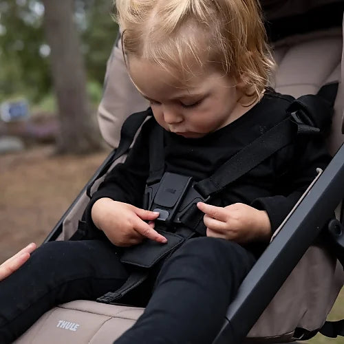 Close-up of child secured in Thule Urban Glide 4-wheel stroller showing padded 5-point harness with magnetic buckle