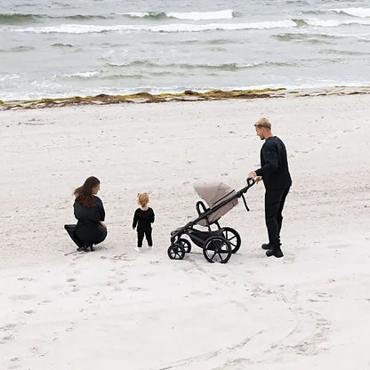 Parents walking on the beach with the Thule Urban Glide 4-Wheel stroller, demonstrating smooth all-terrain performance