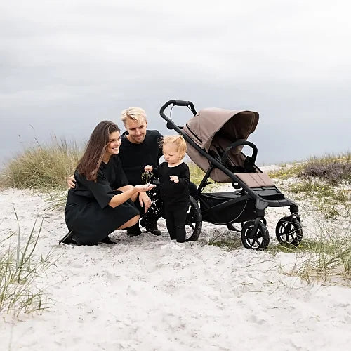 Thule Urban Glide 4-wheel tinted taupe all-terrain stroller with family on the beach