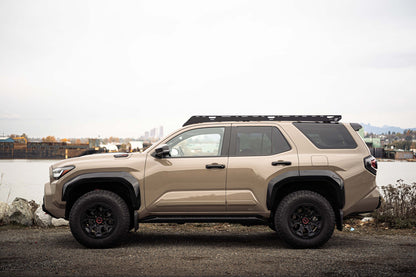 Beige Toyota 4runner with platform roof rack parked near a body of water