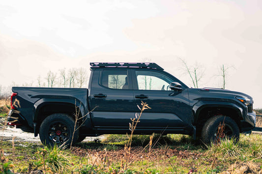 Black pickup truck on a dirt road with a van44 roof rack platform under clear sky background