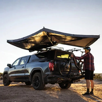 Yakima OverNOut 270 freestanding rooftop awning open on overlanding pickup truck with rear bike rack, creating shaded outdoor shelter for camping and adventure travel in Canada.