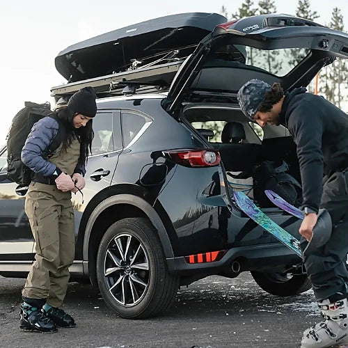Skiers unloading skis from Yakima SkyBox NX Skinny roof cargo box on SUV