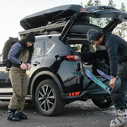 Skiers unloading skis from Yakima SkyBox NX Skinny roof cargo box on SUV